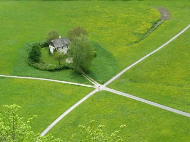Beyond the Crossroads -- Dirt Crossroads next to a house in fields of green grass